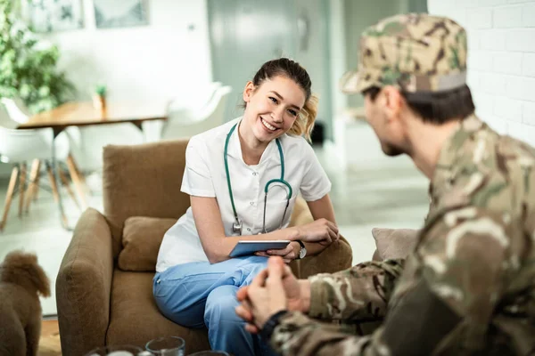 Happy Nurse Using Touchpad Communicating Soldier While Visiting Him Home — Stockfoto