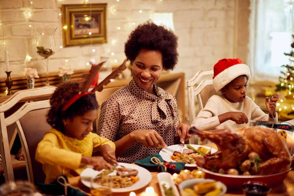 Happy black mother and her children eating Christmas dinner at dining table.