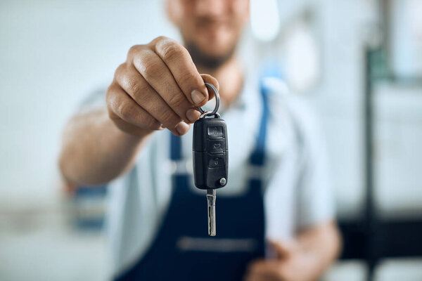 Close-up of mechanic holding key of repaired car at auto repair shop. 