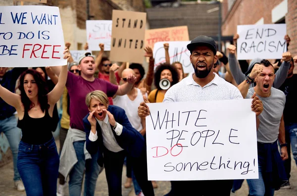 Multi-ethnic crowd of people protesting on anti-racism demonstrations. Focus is on black man holding banner with White People Do Something inscription.