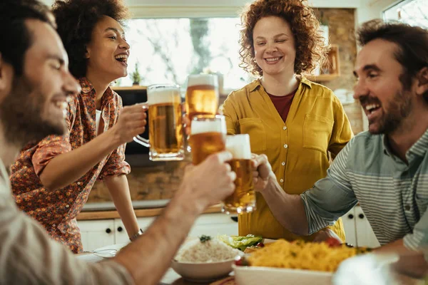 Group of happy friends toasting with beer while having lunch together at dining table at home.  Focus is on women.