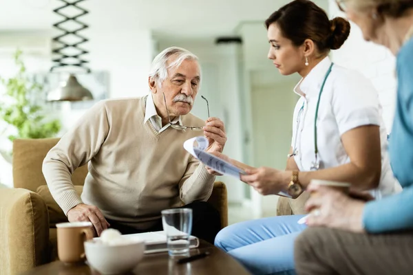 Senior man and healthcare worker going through medical reports during home visit.