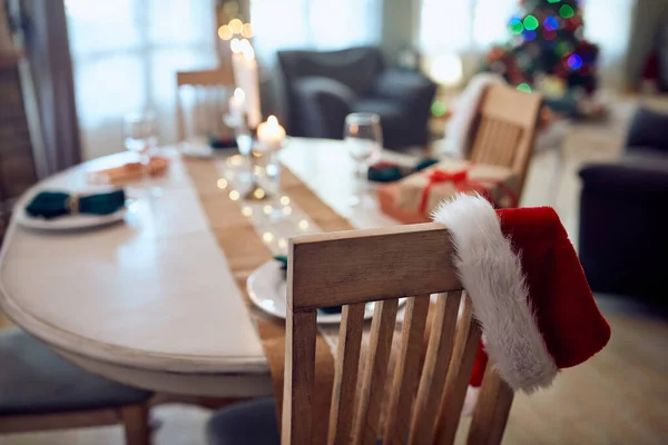 Close-up of dining chair with Santa hat and Christmas table setting at home.