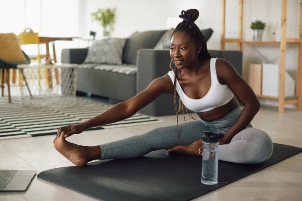 Young black athletic woman stretching on the floor while working out at home.
