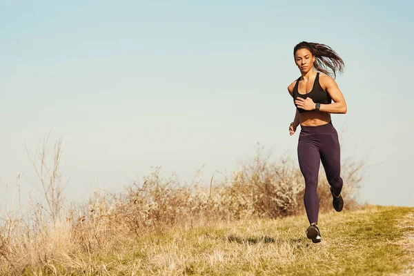 Full length of muscular build sportswoman jogging through the meadow. Copy space.