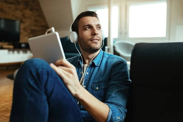 Smiling Man Wearing Headphones Using Touchpad While Relaxing Living Room — Zdjęcie stockowe