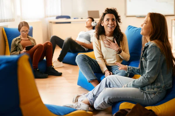 African American high school student gossiping with her female friend while relaxing in the classroom.