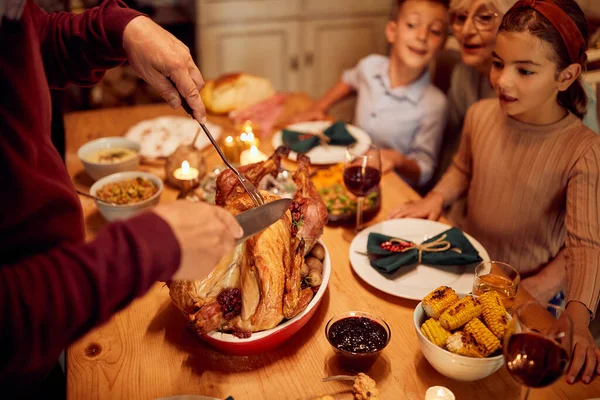 Close-up of grandfather carving turkey meat during Thanksgiving dinner with his family at dining table.