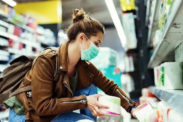 Woman with protective face mask shopping toilet paper in the supermarket during virus epidemic.