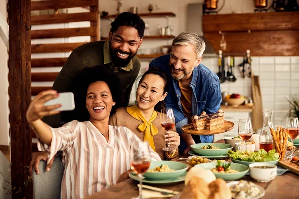 Cheerful multi-ethnic group of friends taking selfie during a meal at dining table.