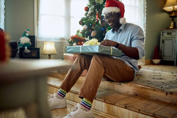 Young Happy Black Man Unwrapping Christmas Gift Home — ストック写真