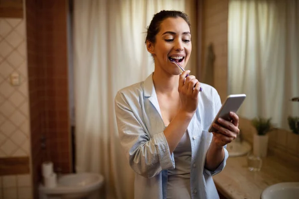 Young Woman Texting Mobile Phone While Brushing Teeth Bathroom — 图库照片