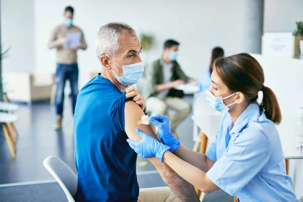 Mature man getting band aid on his shoulder after receiving COVID-19 vaccine at vaccination center.