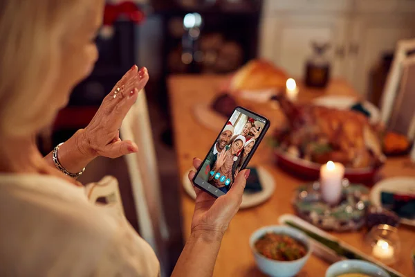 Close-up of mature woman using smart phone and waving to her family during video call on Christmas.