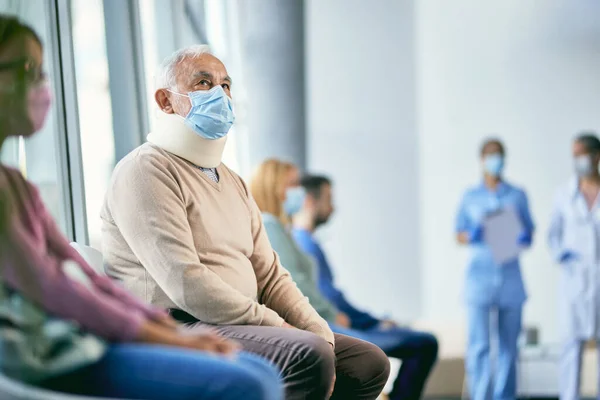 Senior man with injured neck wearing neck brace while sitting at hospital waiting room during coronavirus pandemic.