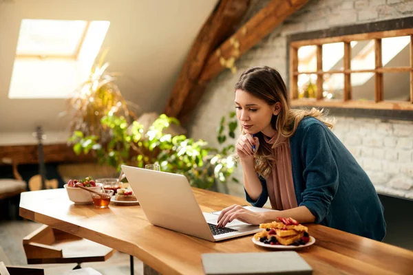 Female entrepreneur reading e-mail on laptop while working from home.