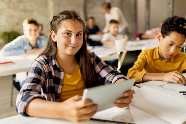 Happy elementary student learning on touchpad in the classroom and looking at camera. 