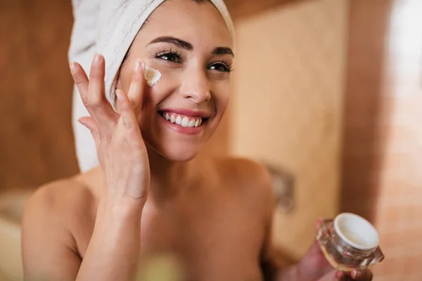 Beautiful Woman Wrapped Towel Applying Face Cream Bathroom — стоковое фото