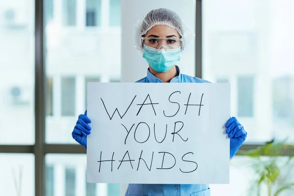 Healthcare worker holding placard with wash your hands text as appeal during virus epidemic.