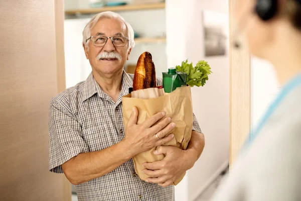 Happy Senior Man Standing Doorway Holding Bag Groceries While Talking — Stockfoto