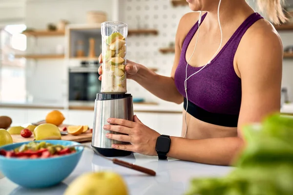 Unrecognizable athletic woman using blender while making fruit smoothie in the kitchen. 
