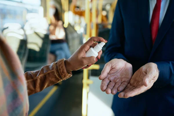 Close-up of two people disinfecting hands while commuting by bus.