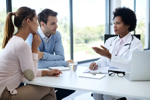 Black female doctor talking to a couple while having appointment at clinic.