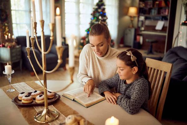 Mothers and daughter reading Hebrew bible while celebrating Hanukkah at home.