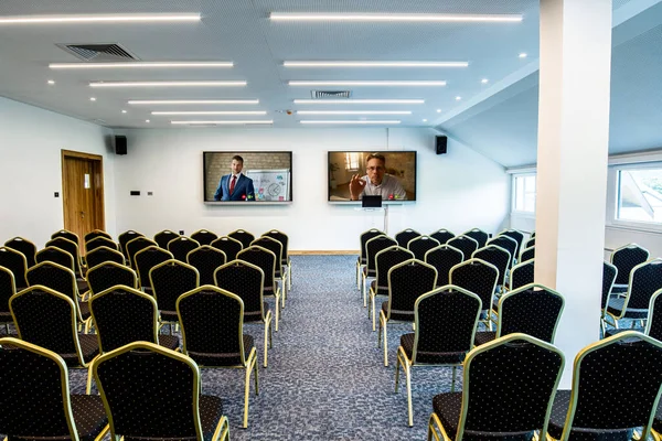 Two businessmen on projection screens in empty conference hall.