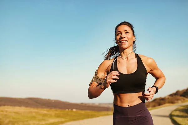 Determined muscular build woman running while exercising in nature. Copy space.