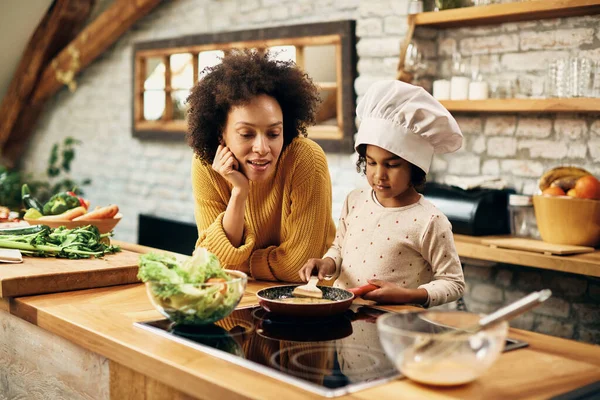 Small black girl preparing food with her mother in the kitchen.