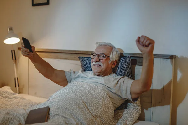 Happy mature man cheering while watching sports match on TV in bedroom.