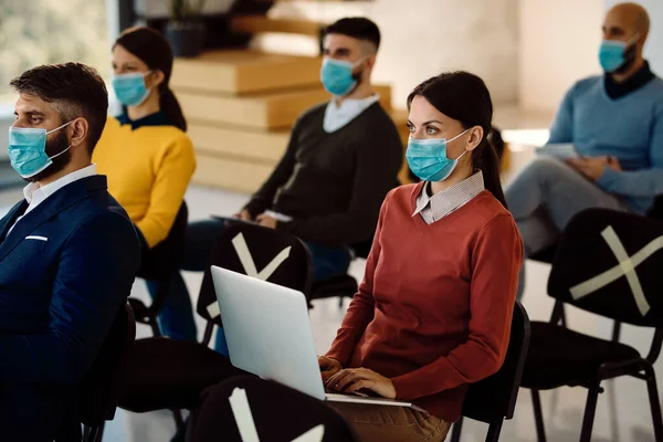 Group of entrepreneurs with protective face masks attending a seminar in board room. Focus is on businesswoman using laptop.