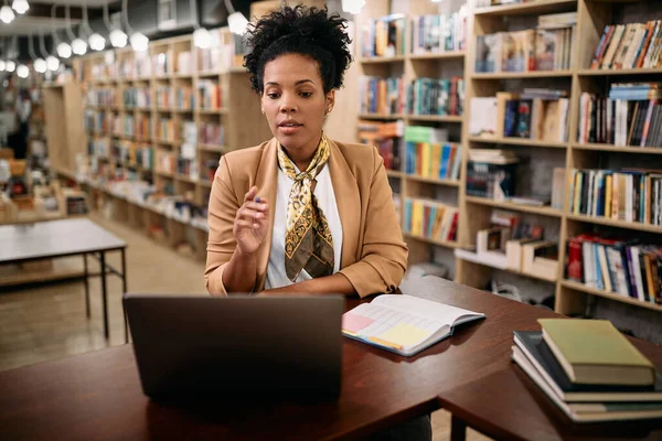 African American female professor using laptop while holding online class in a library,