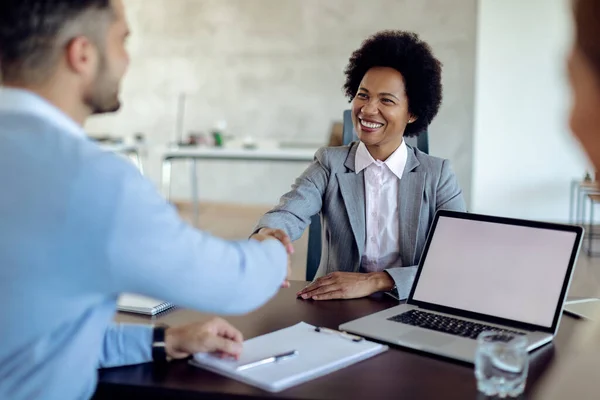 Happy African American financial advisor shaking hands with her client after successful agreement in the office. 
