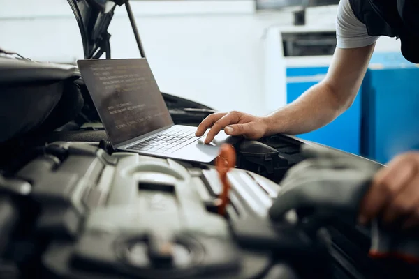 Close-up f mechanic running diagnostic on laptop while analyzing engine problems at car service workshop.