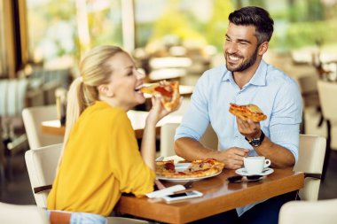 Happy couple having fun while eating pizza in a restaurant. Focus is on man. 