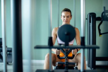 Dedicated athletic woman having cross training on rowing machine in health club. Copy space. 