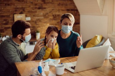Distraught parents communicating with a doctor via video call while taking care of their ill daughter at home during COID-19 pandemic.