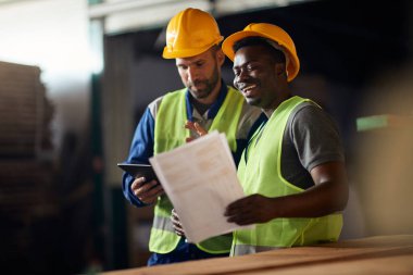 Happy manual workers going through delivery checklist while working at distribution warehouse.