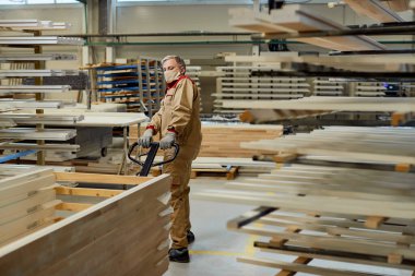 Full length of manual worker with face mask pulling pallet jack at carpentry workshop.