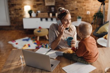 Happy mother making a phone call while babysitting her small son and working at home. 