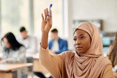 Female Islamic student raising her arm to ask a question during lecture in the classroom.