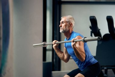 Mature athletic man lifts barbell while exercising strength in g