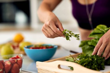 Close-up of woman using parsley while making healthy food in the kitchen. 
