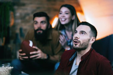 Young man watching sports match on TV with his friends at home,