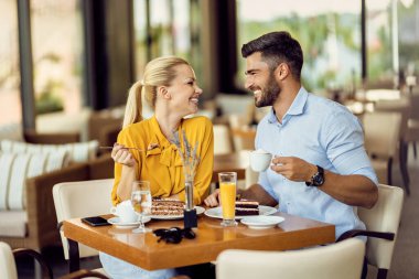 Happy couple communicating while enjoying in cup of coffee and dessert in a cafe.