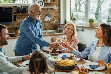 Happy multi-generation family having lunch together in dining room. Senior man is tasting with his adult daughter. 