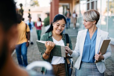 Happy Asian student communicating with her professor in front of university building.