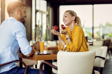 Happy couple enjoying while relaxing in a cafe and talking. Focus is on happy woman eating a donut. 